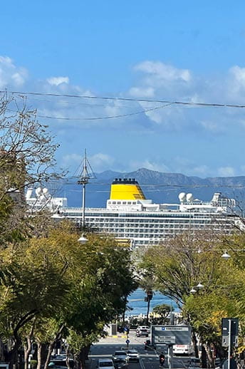 A view of the ship in port, through the trees, from a hilltop street in Cagliari, Italy